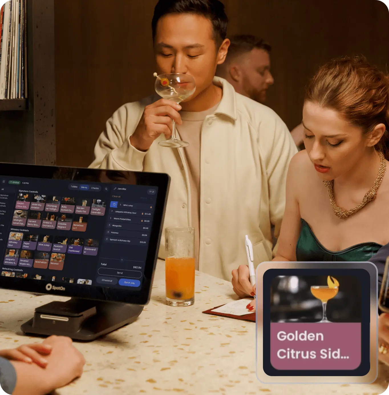 The image features a lively bar scene where a man enjoys a cocktail, while a woman in an elegant dress is writing beside a table equipped with a sleek touchscreen, possibly in SpotOn, Bradenton, FL.