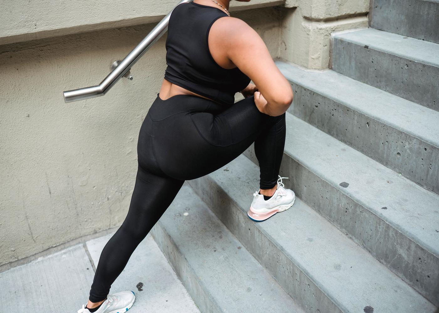Woman in workout clothes outside stretching on staircase