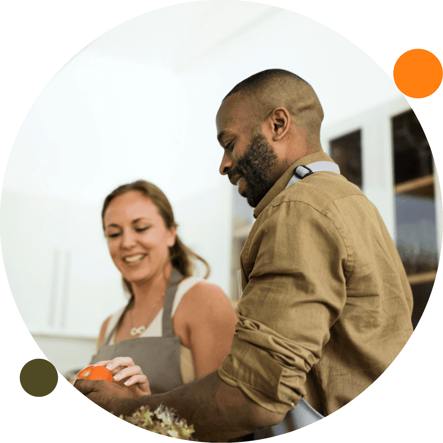 Two people in aprons smile while preparing food together in a bright kitchen