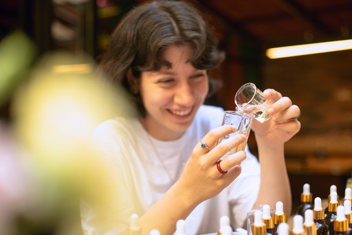 A person crafting a Turkish mosaic lamp, carefully applying multicolored beads to the ornament. The background shows a workshop setting with tools hanging on the wall.