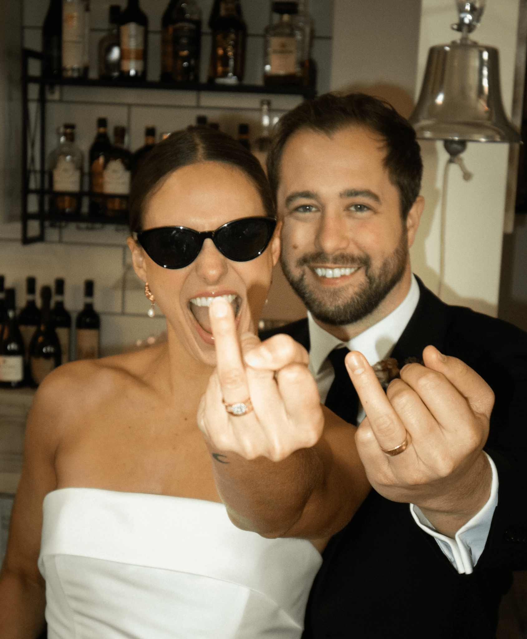 Bride and groom showing off wedding bands in front of stocked bar at Ashlar Ottawa