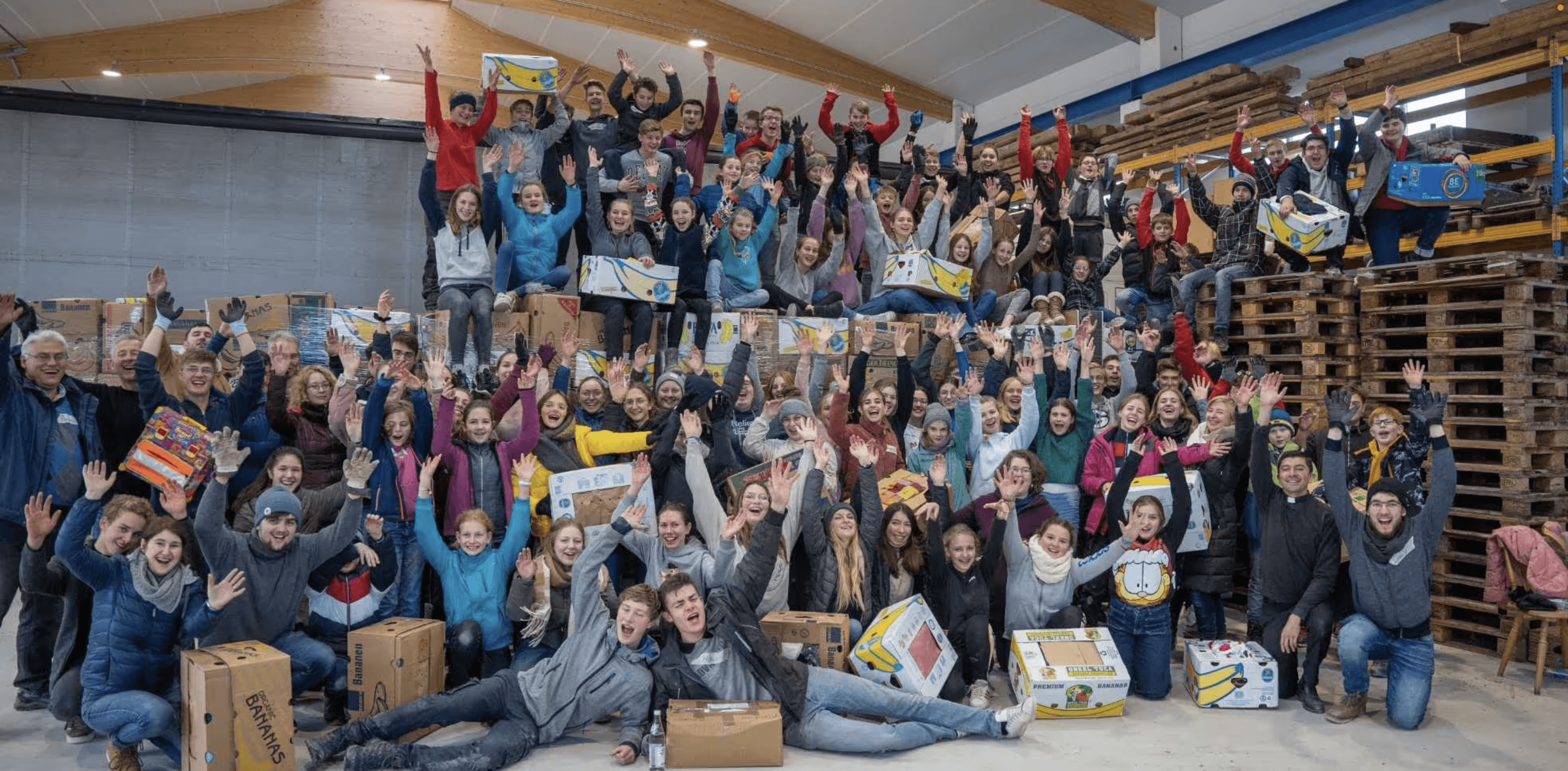 Gruppenbild vieler Helfer von Junge Leute Helfen in einer Lagerhalle die jubeln
