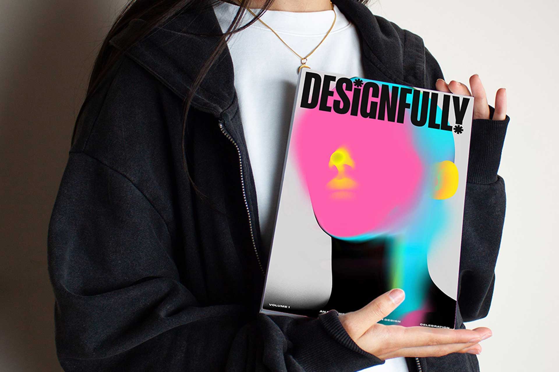 Woman in a black hoodie holding a copy of Designfully magazine with an abstract pink and blue cover