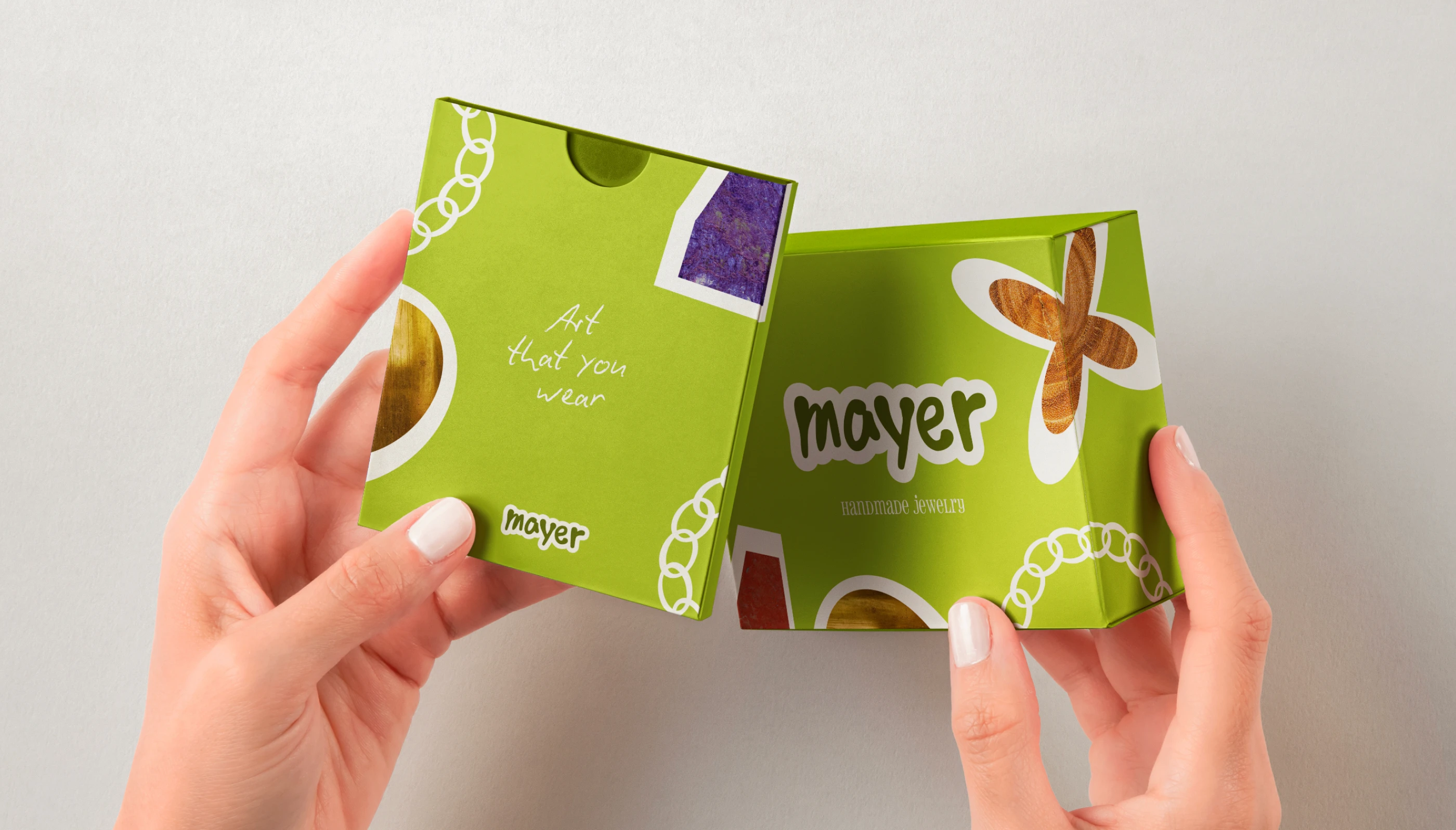Mise en situation du packaging Mayer Jewelry tenu à la main. Boîtes à bijoux colorées avec motifs artistiques et logo sticker.