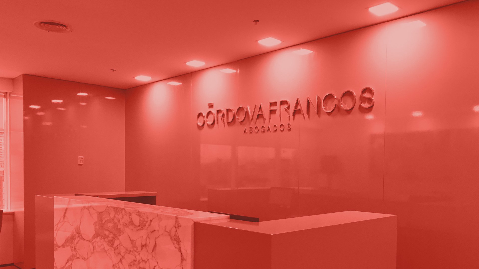 A sleek, modern office lobby with red lighting, featuring a marble reception desk and signage reading "Córdova Francos Abogados" on a glossy wall.