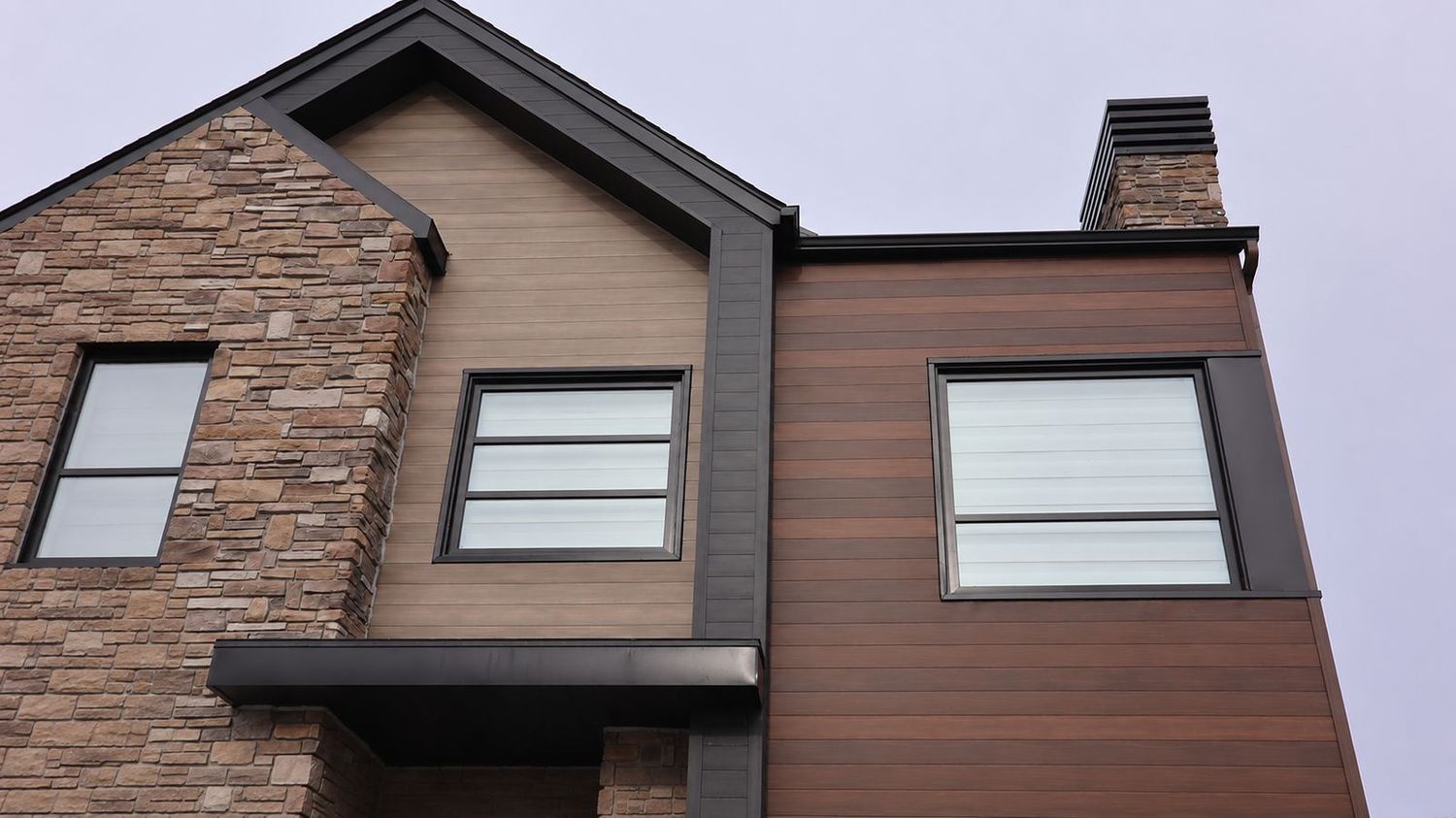 Esquina de fachada que combina piedra vista con metal siding símil madera en dos tonos y aberturas en negro
