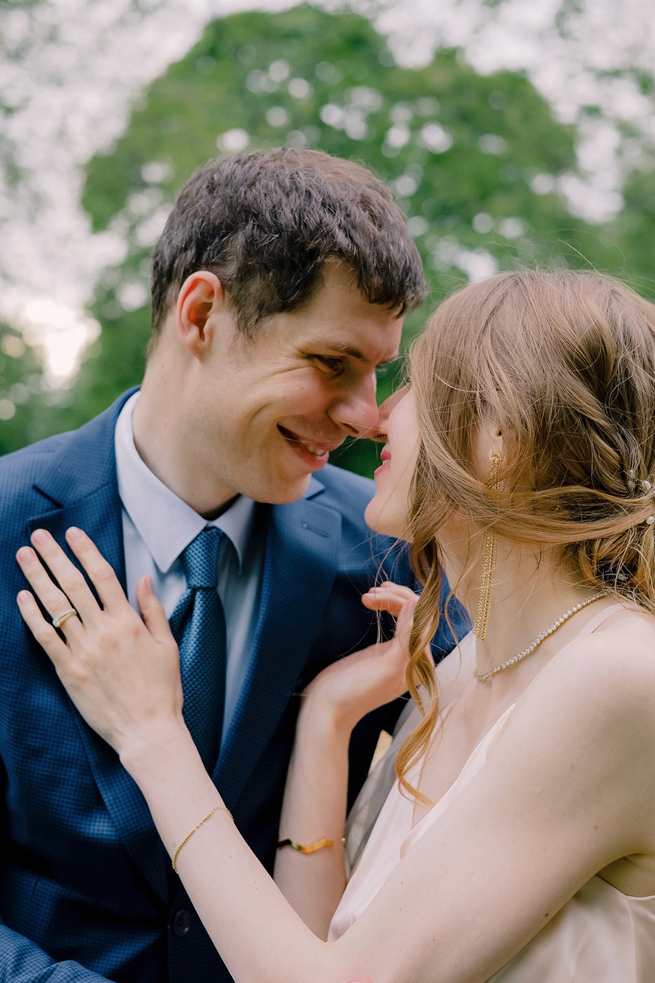 Romantic outdoor wedding portrait of a couple sharing an intimate moment in elegant formalwear surrounded by soft natural greenery