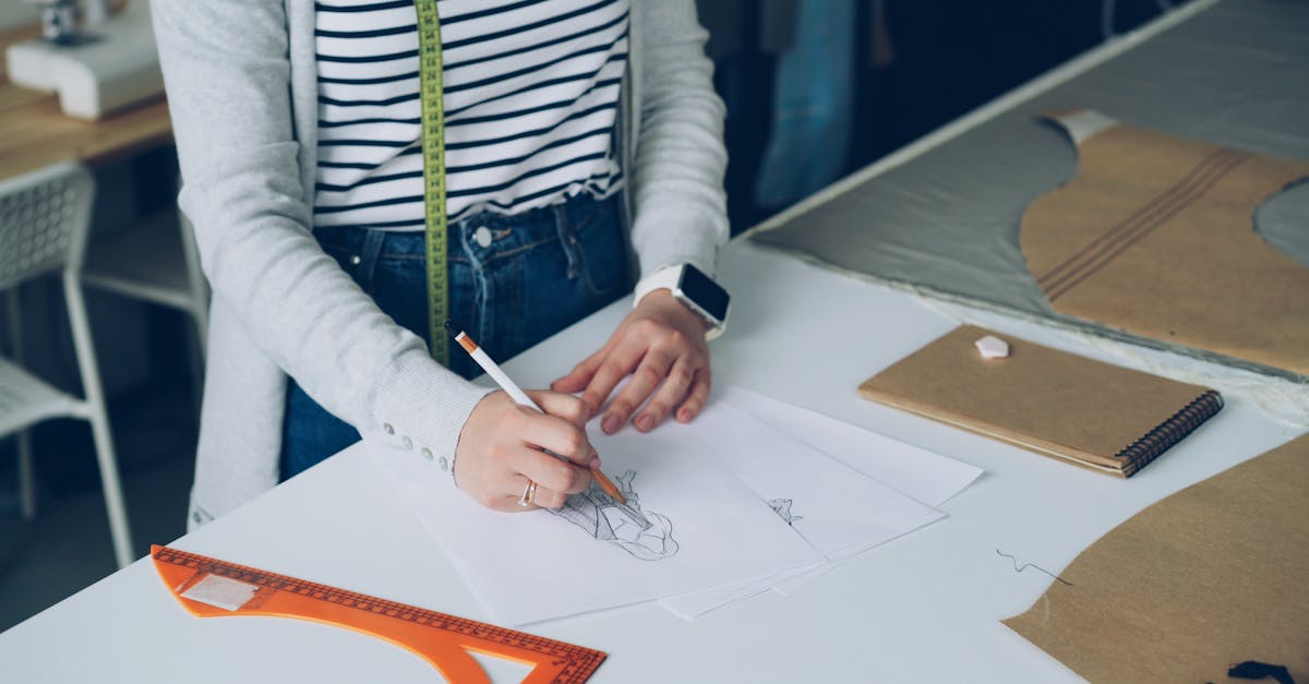 A designer drawing fashion sketches at a desk with sewing patterns in a studio.