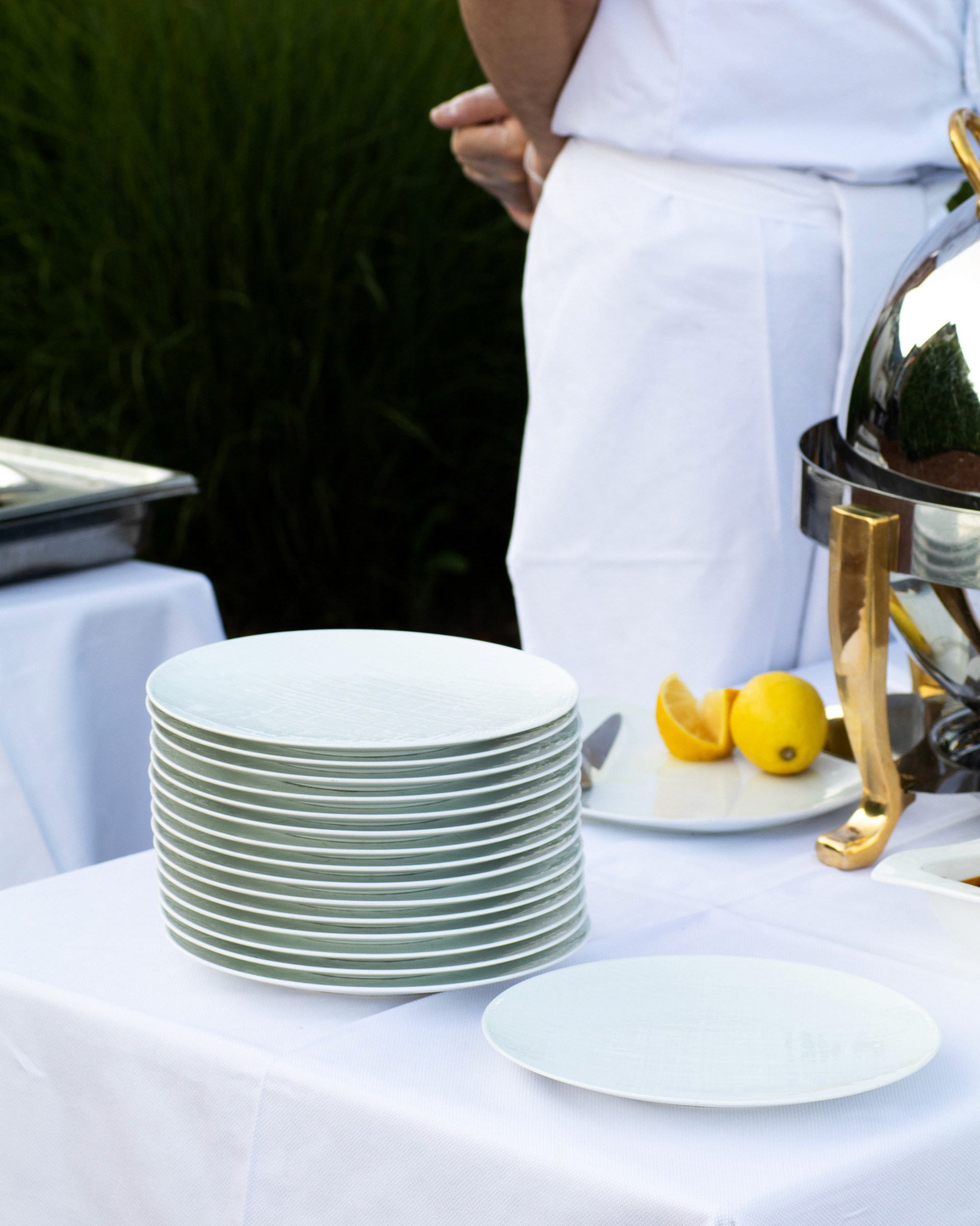 Gros plan sur l'angle d'un buffet où sont empilées des assiettes blanches prêtent à être remplies par l'un des cuisiniers que l'on aperçoit au second plan de l'Hôtel Palafitte