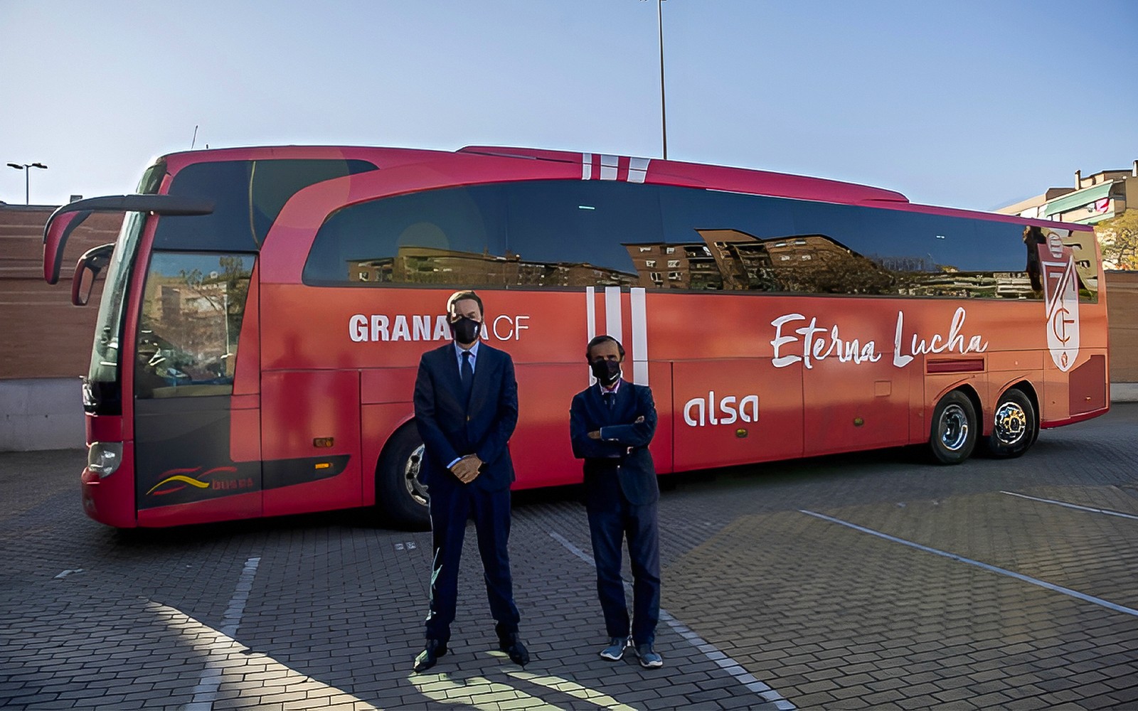 Personal de pie frente al autobús rojo de traslado Alsa del Aeropuerto de Granada.