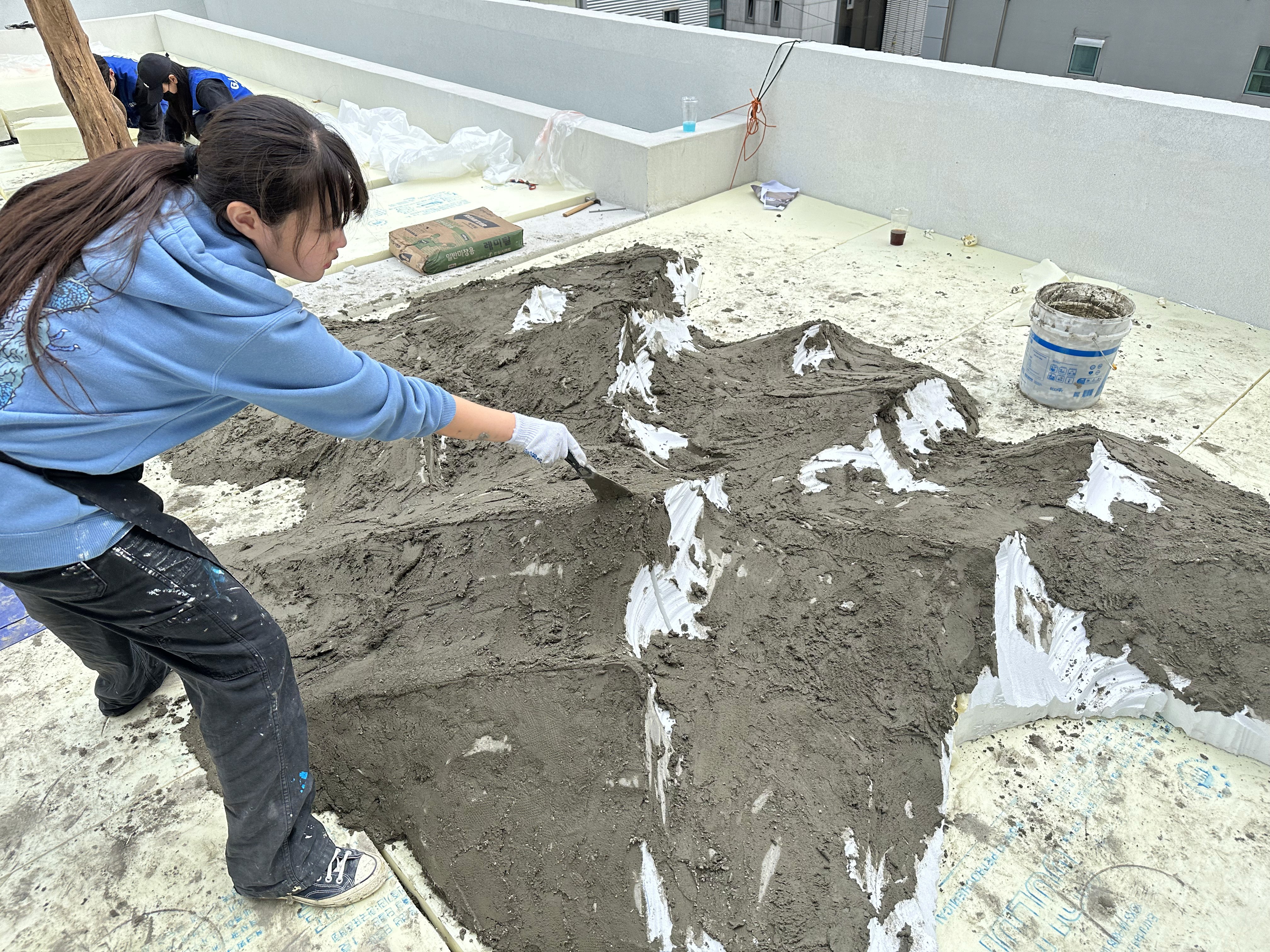 시멘트를 손으로 직접 도포하여 조형물 표면을 마감하는 과정 / Hand-applying cement finish to the sculpture surface