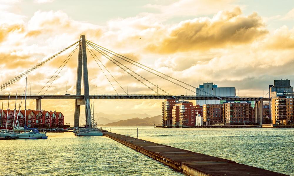Man with glasses and an AirPod in his ear working on a laptop at a desk next to another person.