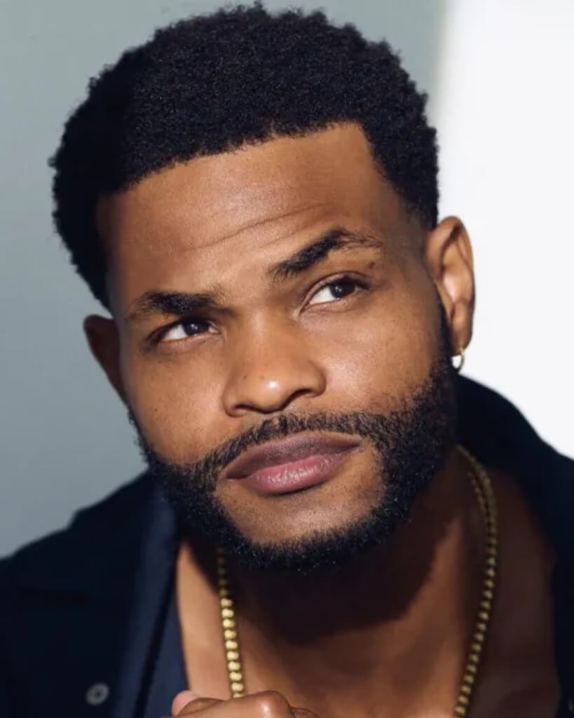 MrBeast, a young man with short hair wearing a black t-shirt, looking thoughtfully to the side against a gray background.