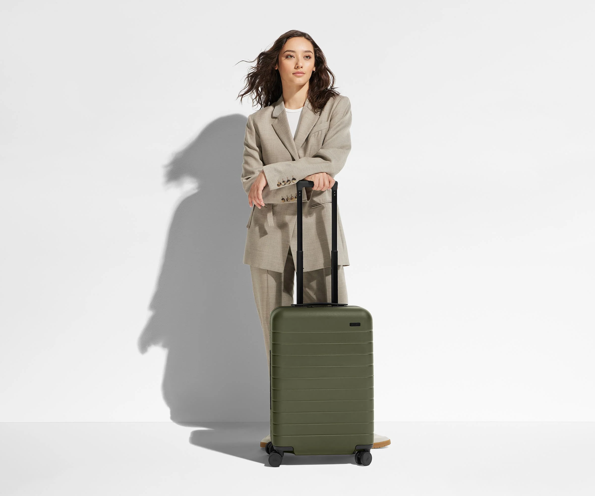 Woman standing with a green suitcase against a light background