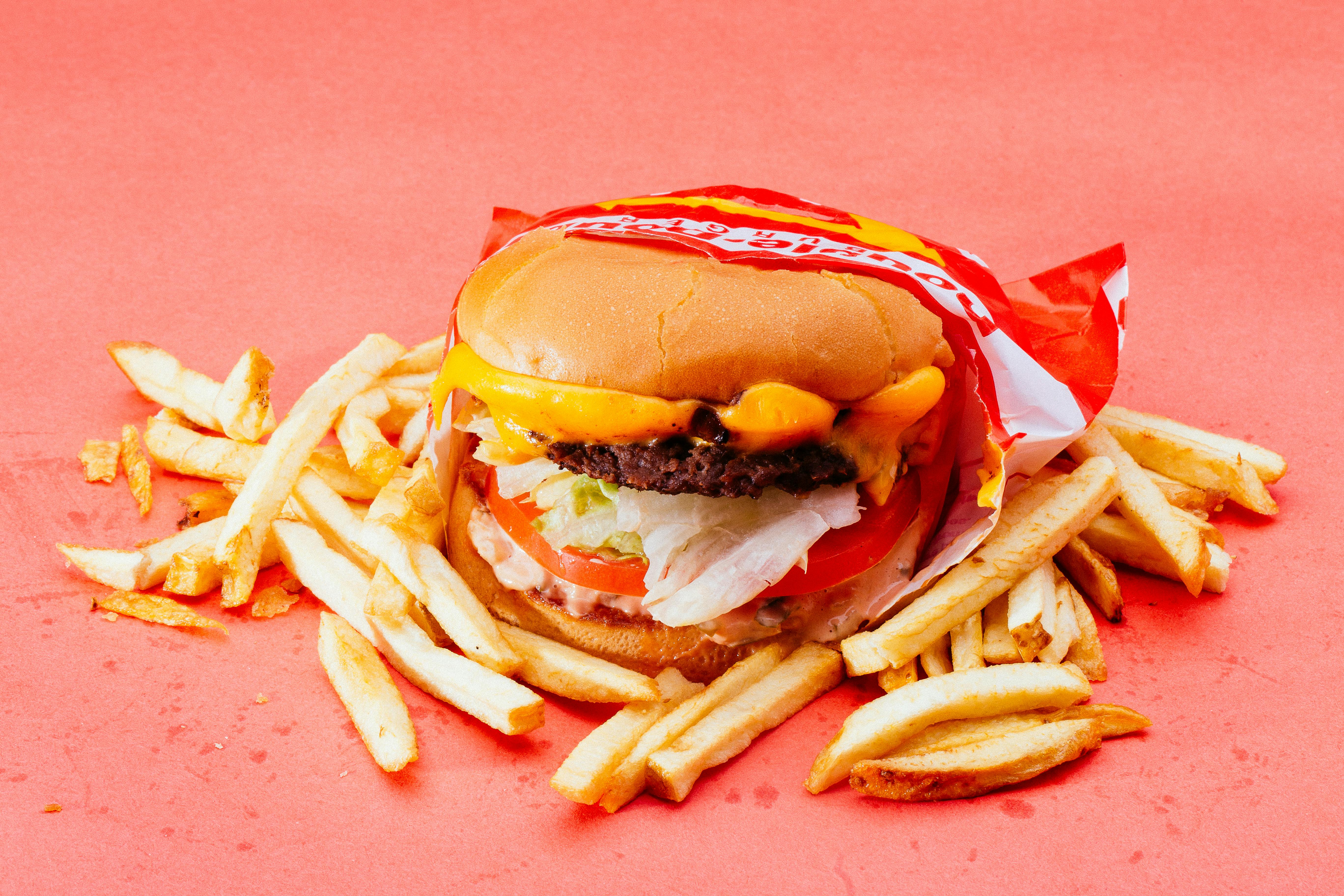 Ultra-processed fast food burger and chips on an orange background