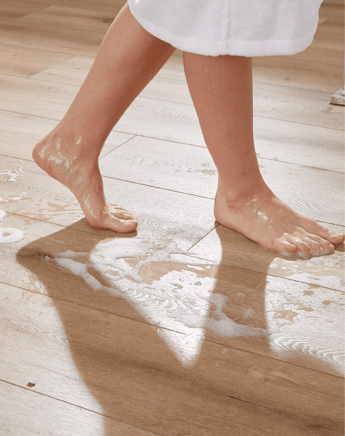 赤腳在濕滑有肥皂泡的木紋膠地板上行走，展示SPC石塑地板防水防滑性能，是香港家居裝修首選防水地板材料。