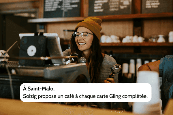 Photo d’une barista souriante à Saint-Malo servant un café, illustrant une offre Gling locale où Soizig offre un café pour chaque carte de fidélité complétée.