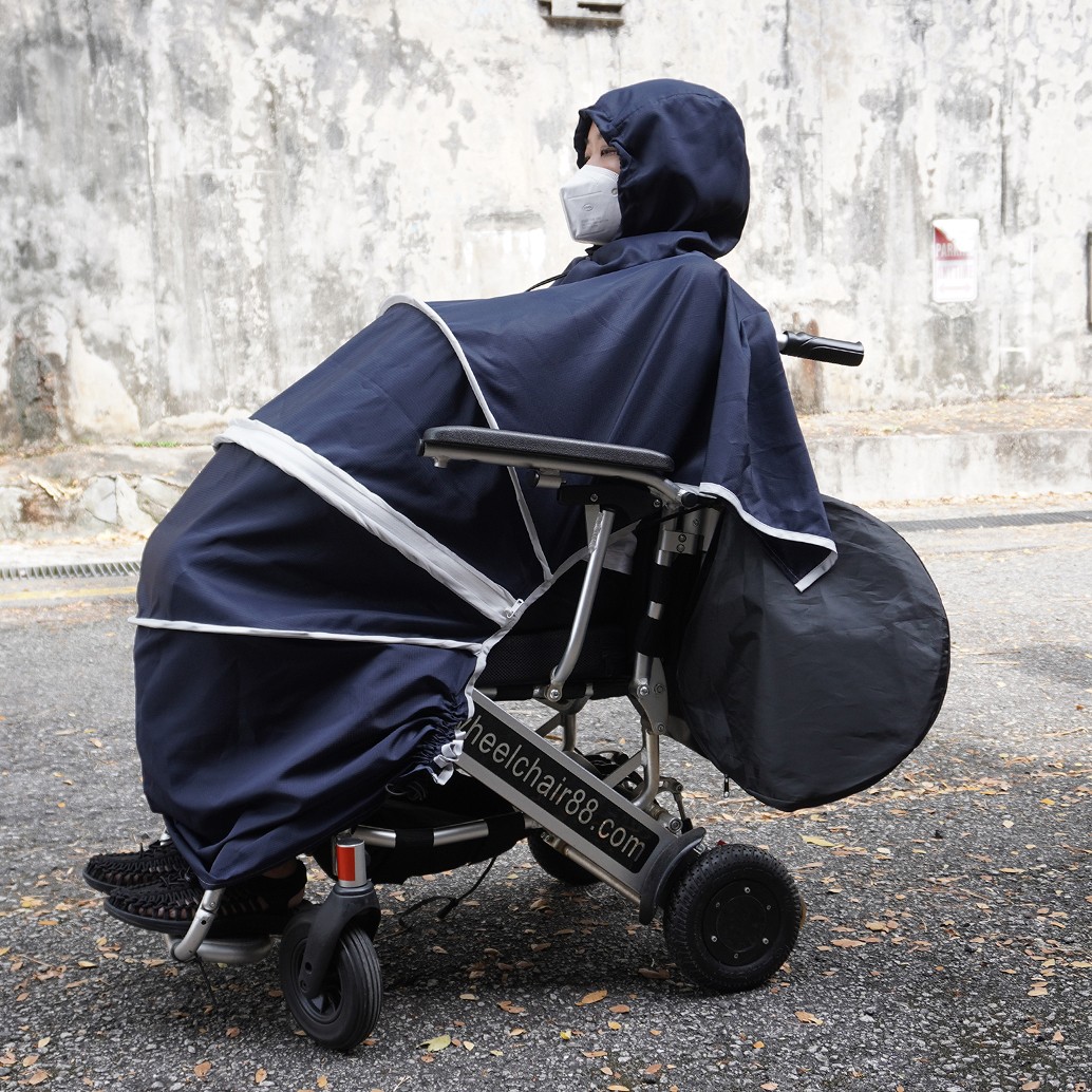 Side view of a wheelchair user seated on a wheelchair outdoors, wearing the 55 Minutes Wheelchair Poncho