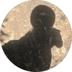 Editorial portrait of a young man with wavy hair in a knit sweater, looking over his shoulder in soft light.