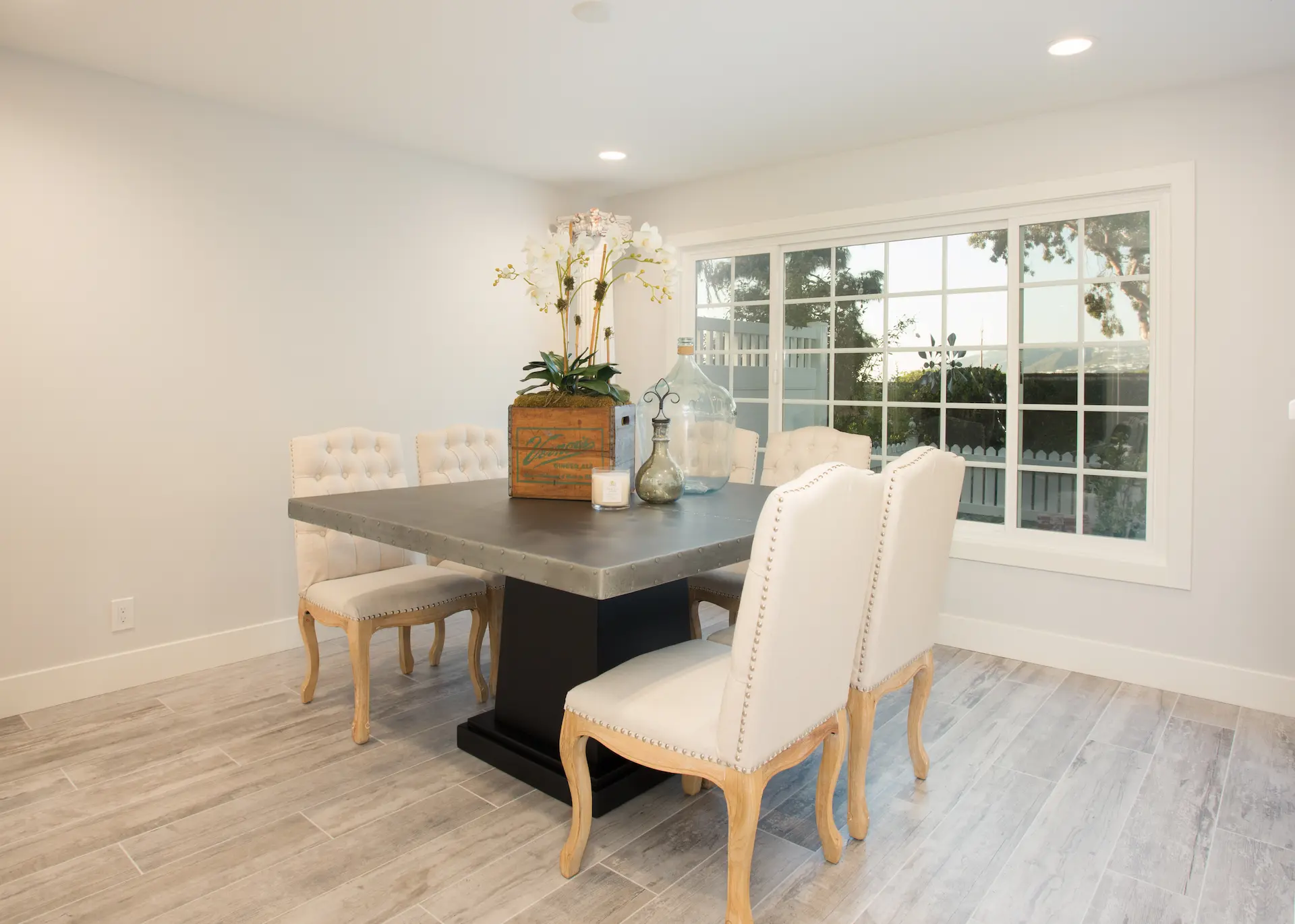 Elegant dining area with large window, grey stone table, tufted chairs. From Dana Point Cape Cod remodel, photo by Chris Darnall