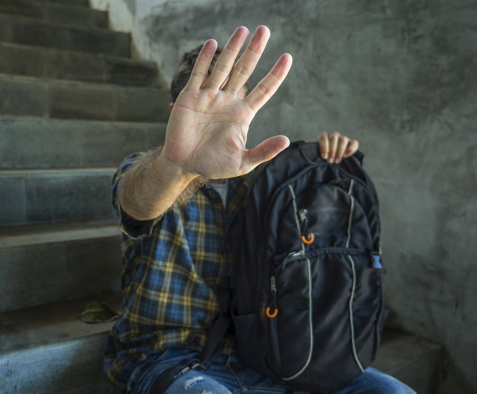 A person sitting on stairs holding up their hand in a "stop" gesture, with someone placing a hand on their shoulder from behind.