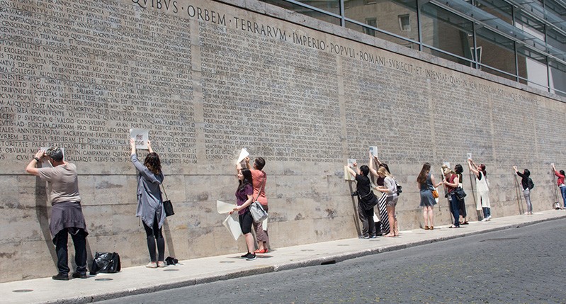 people making frottage on letters on roman wall