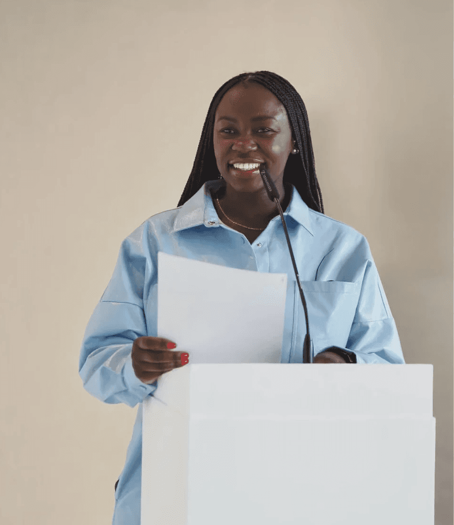 Mary smiling while standing on a stage, giving a speech to an audience
