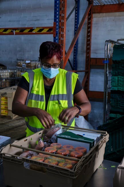 A warehouse worker in safety gear packing food parcels for distribution.