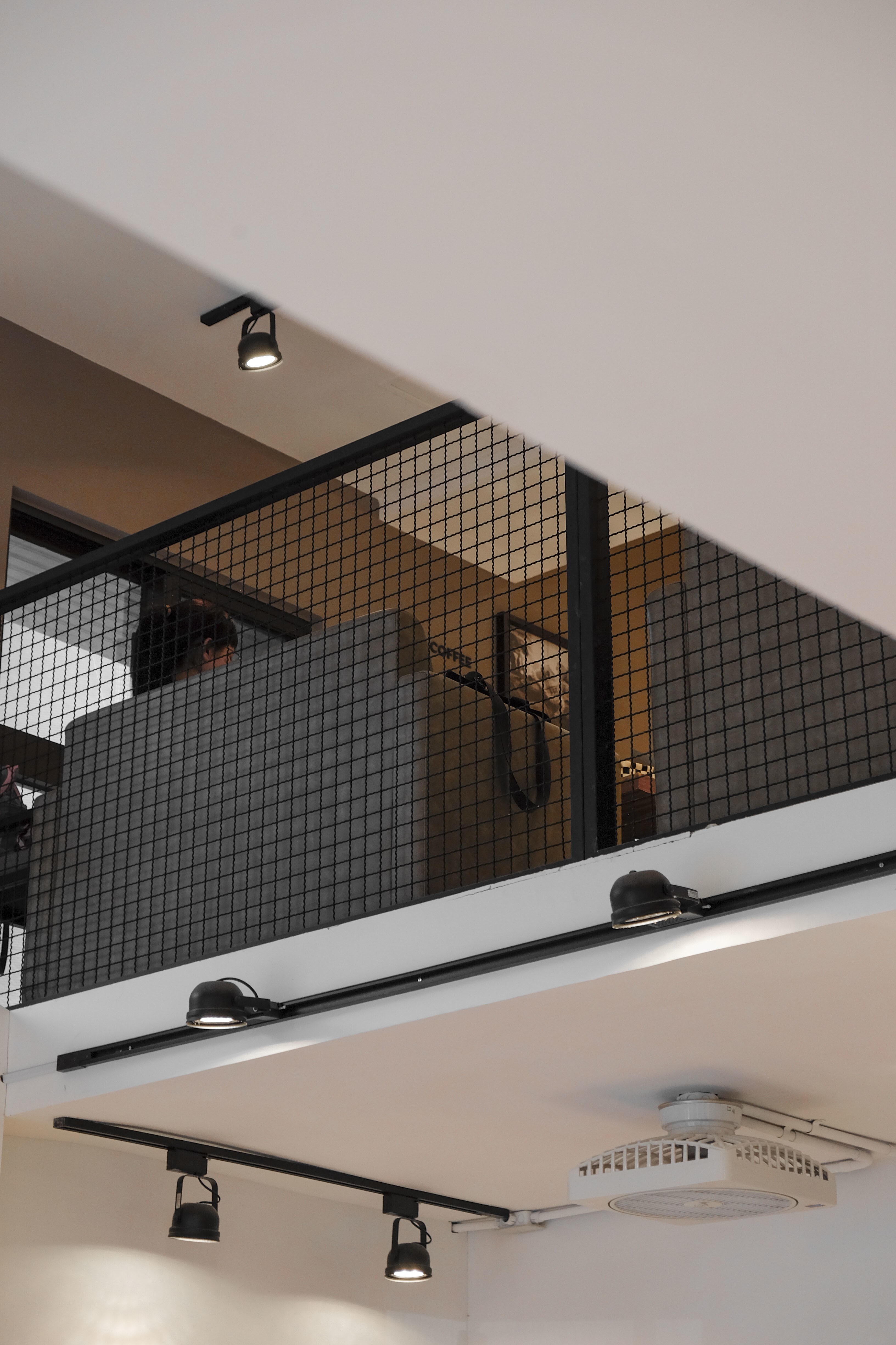 A modern interior with two levels, featuring black metal railings for an overhead ceiling rack and lighting fixtures. 