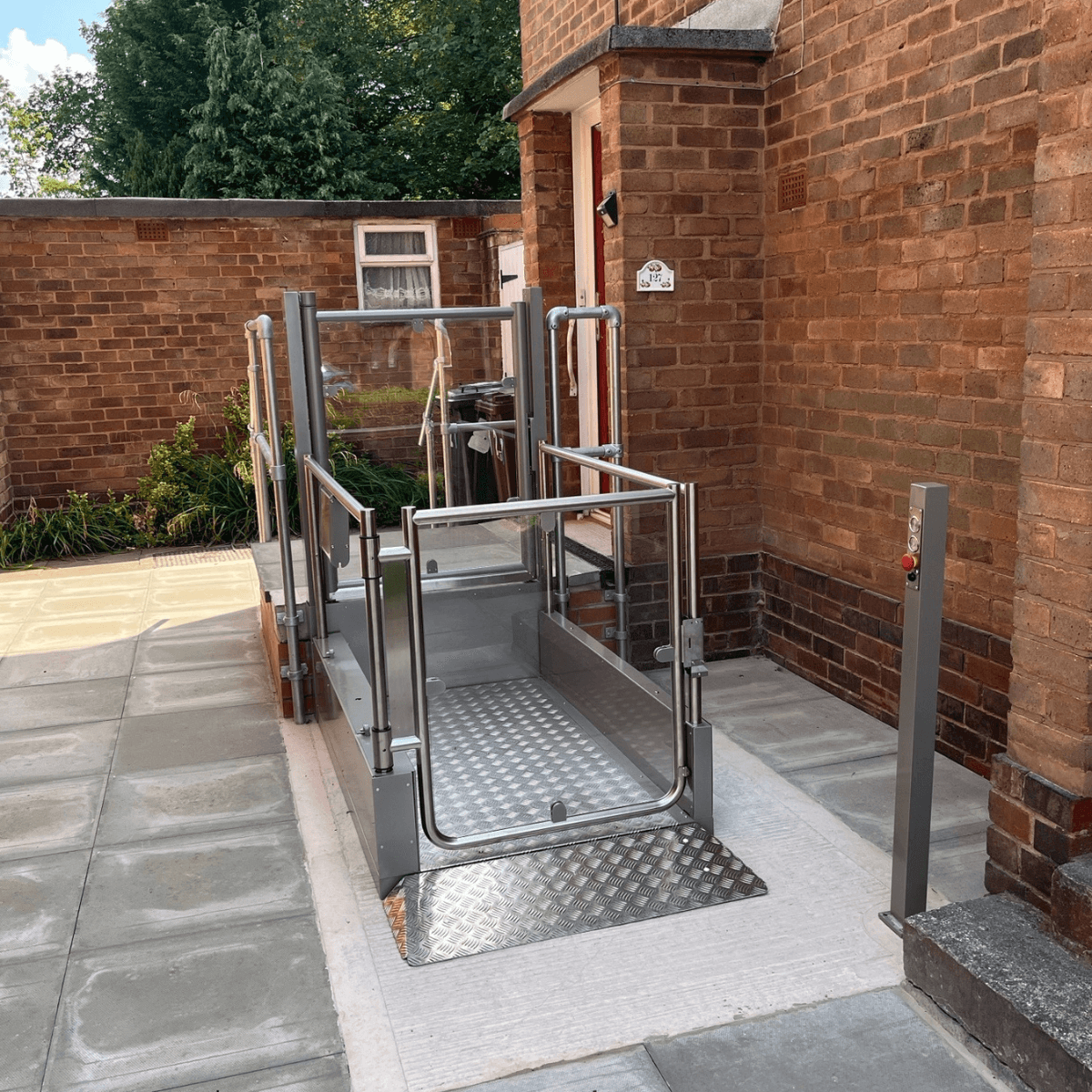 An outdoor step lift installed at a UK residential property in Wolverhampton, showing the open platform, stainless steel safety enclosure, entry ramp, and external call post at ground level.