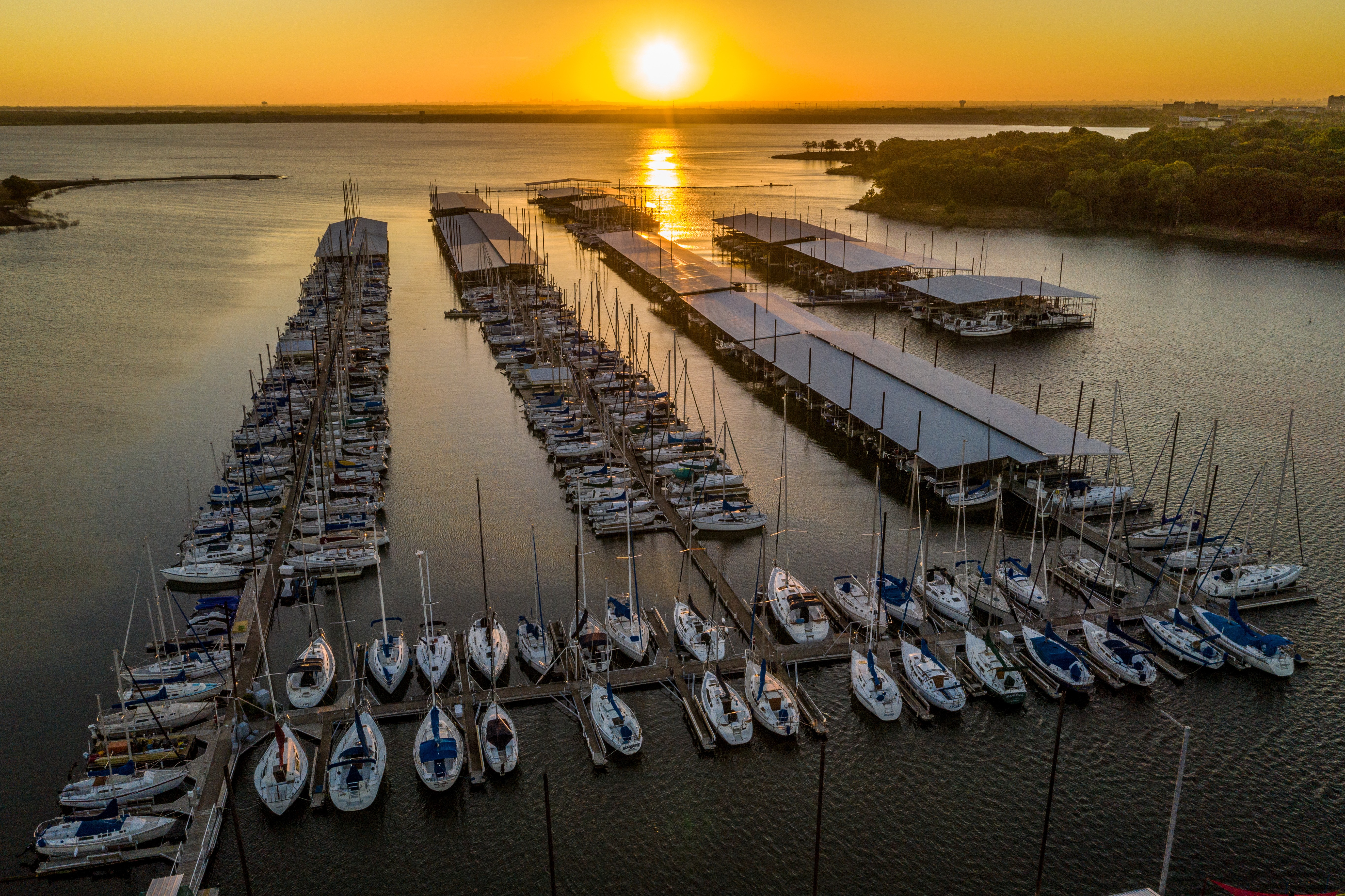 Sunset over a serene scott's landing marina with rows of sailboats and yachts docked along wooden piers, reflecting golden hues on the calm water; scenic view of a vibrant sky enhancing a peaceful waterfront setting.