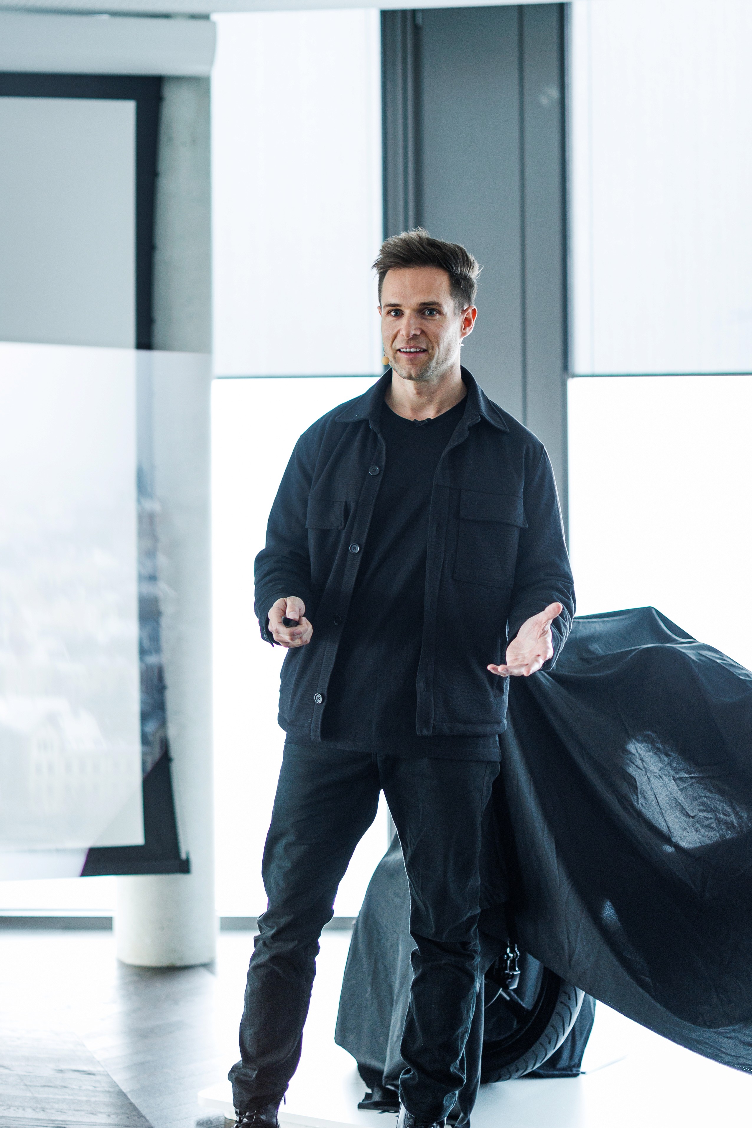 Smiling person with curly hair, wearing a black shirt, against a warm, dark background.