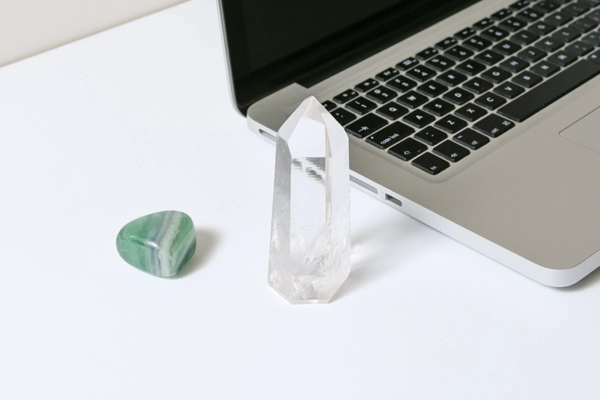 Clear Quartz point and Fluorite tumbled stone on desk beside laptop