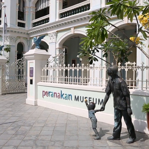Exterior of the Peranakan Museum with bronze statues of a man and child holding hands near the entrance gate.