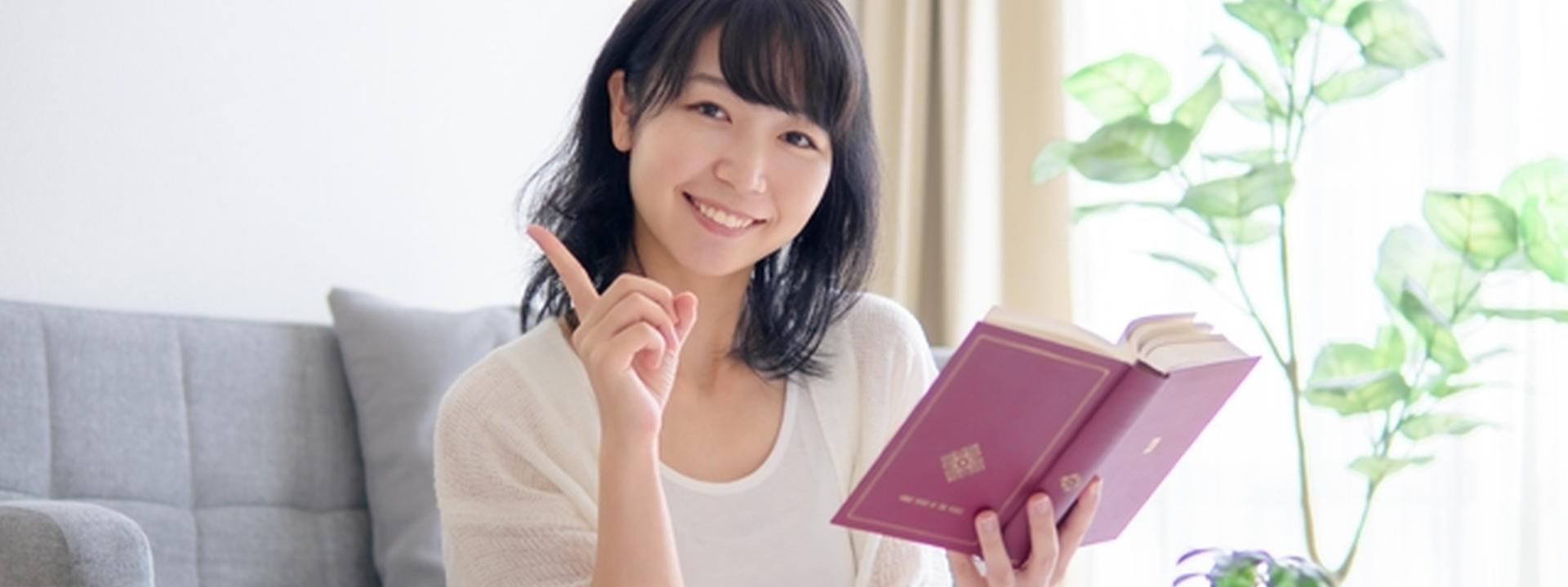 本を読みながら指を立てて微笑む女性