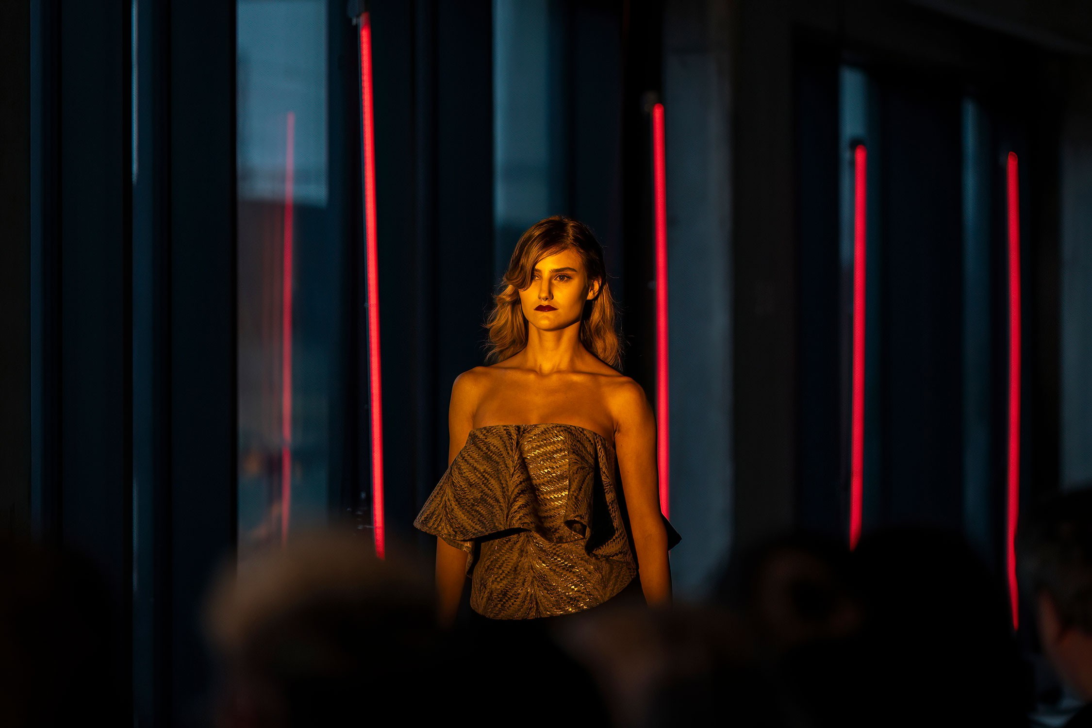 Fashion photoshoot featuring a model on stage under dramatic lighting.