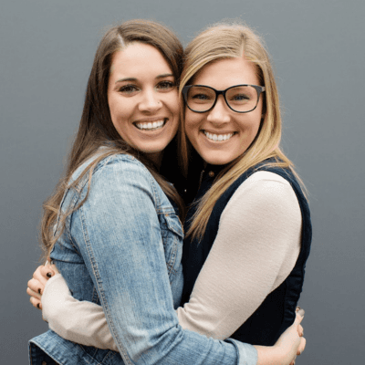 A thoughtful person with long blonde hair wearing a ruffled orange shirt against a vibrant orange background, rests their chin on their hand with a curious expression.