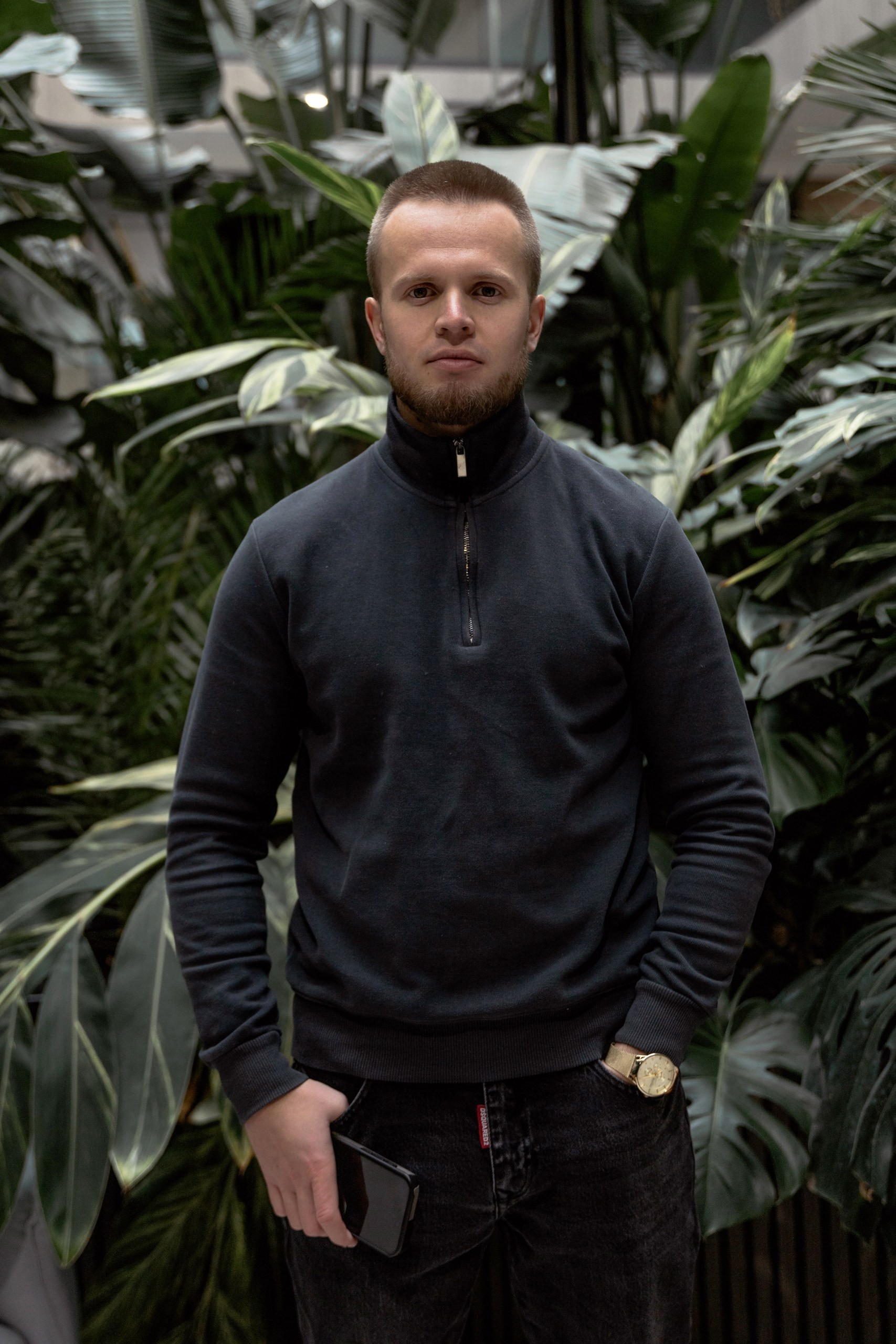 Casual studio portrait of a bearded man with curly hair in a white shirt, arms crossed, on a light gray background.