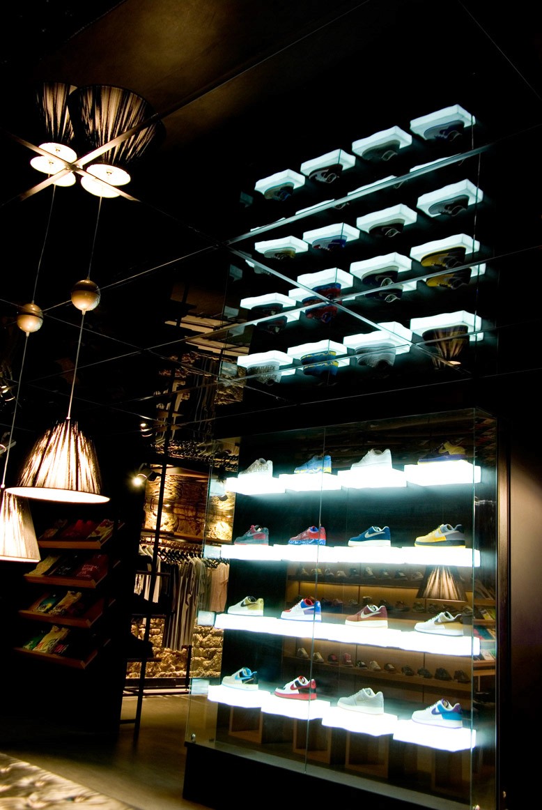 Illuminated sneaker display at Apartment Store with mirrored ceiling, glowing glass shelves, and warm ambient lighting reflecting the basement interior.
