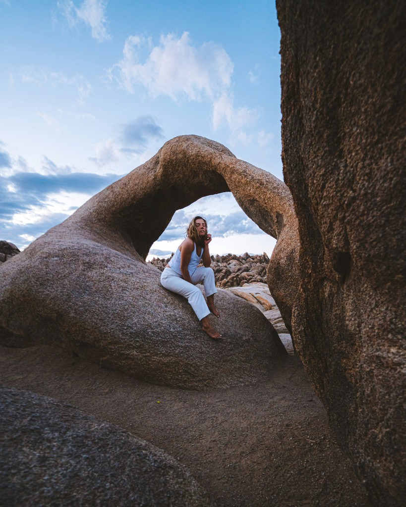 A woman sitting under a brown arch rock formation