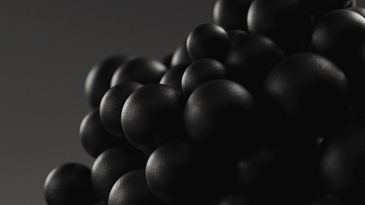 A close-up of several smooth, dark spheres grouped together. The lighting creates soft highlights and deep shadows on their rounded surfaces, giving them a sleek, metallic, or molecular appearance.