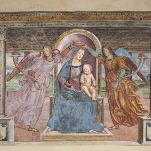 A woman sitting with a child on her lap is crowned by two angels under a decorative ceiling.
