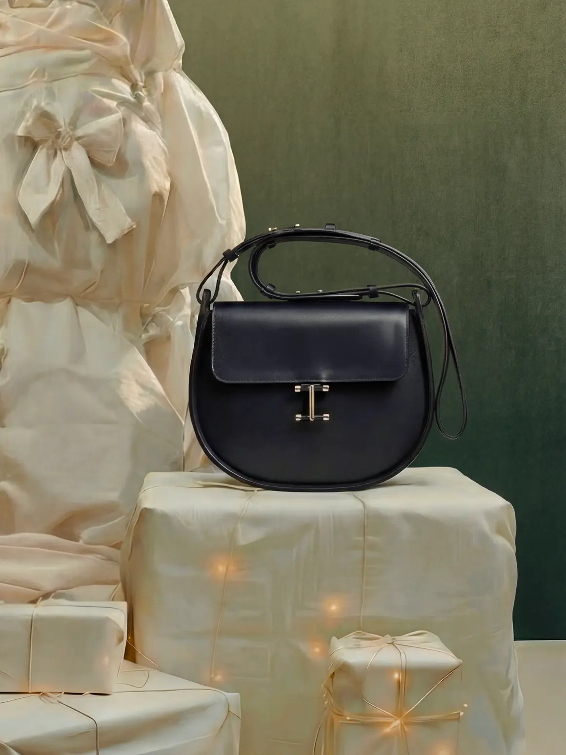A sleek black leather handbag with a polished metal clasp is elegantly displayed on a fabric-draped pedestal surrounded by wrapped gift boxes, embodying a high-end fashion brand aesthetic.