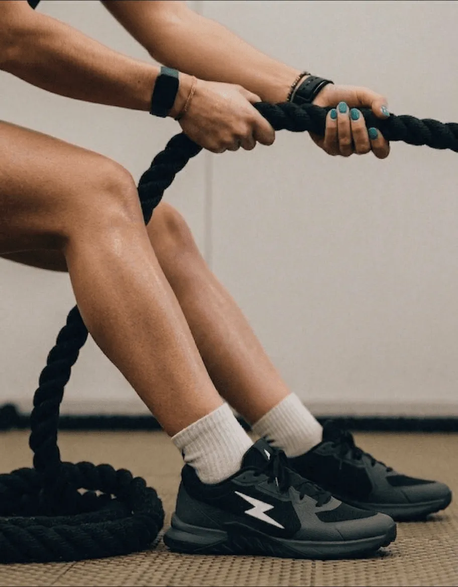 Close-up of woman's hands and legs gripping battle ropes during high-intensity workout wearing black sneakers and white socks