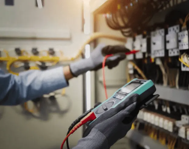 Technicien utilisant un multimètre pour vérifier des connexions électriques dans une armoire de contrôle.