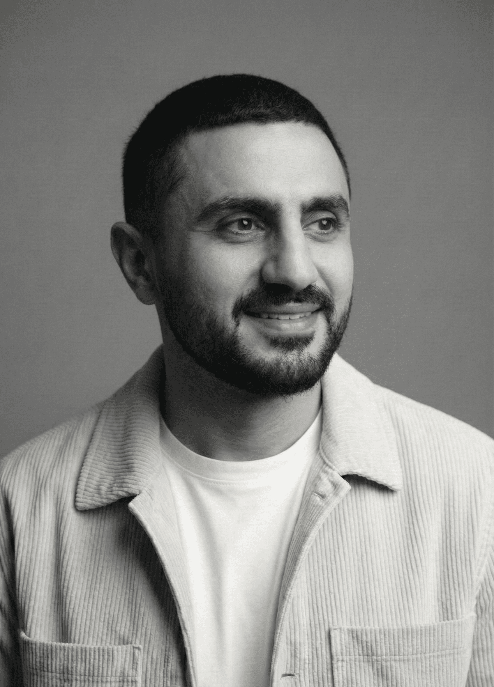 Portrait of a young man with short hair, wearing a dark t-shirt, against a plain background.