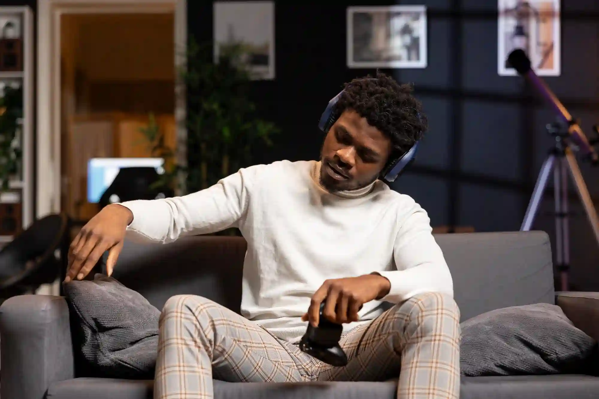 Man with headphones holding a game controller and relaxing on a couch.