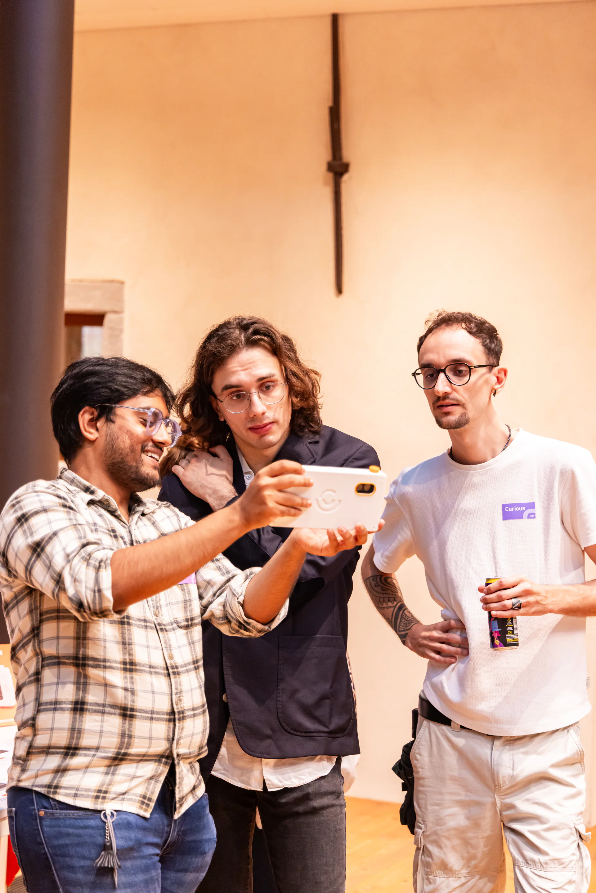 Three people gather around the screen of a white handheld camera prototype.