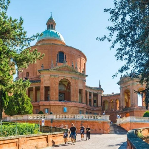 Grande edificio rotondo di colore terracotta con una cupola, circondato da alberi. Persone camminano sul vialetto che conduce all'ingresso.