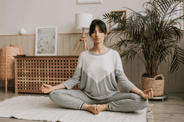 Young woman sitting cross-legged and meditating at home